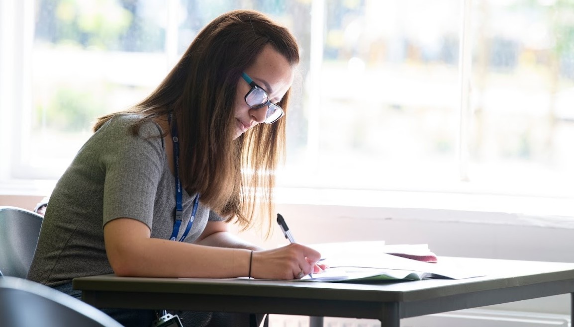 A woman sitting at a desk writing in her notebook