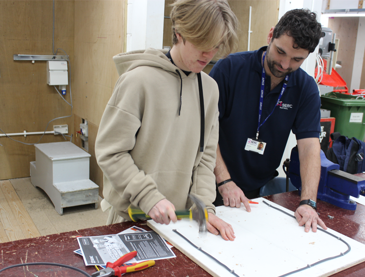 aspiring electrician practicing skills with lecturer looking on