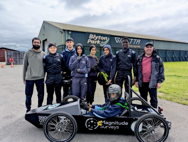 A group of Bradford school pupils pose on a race track next to the Greenpower kit car they built ready to race.