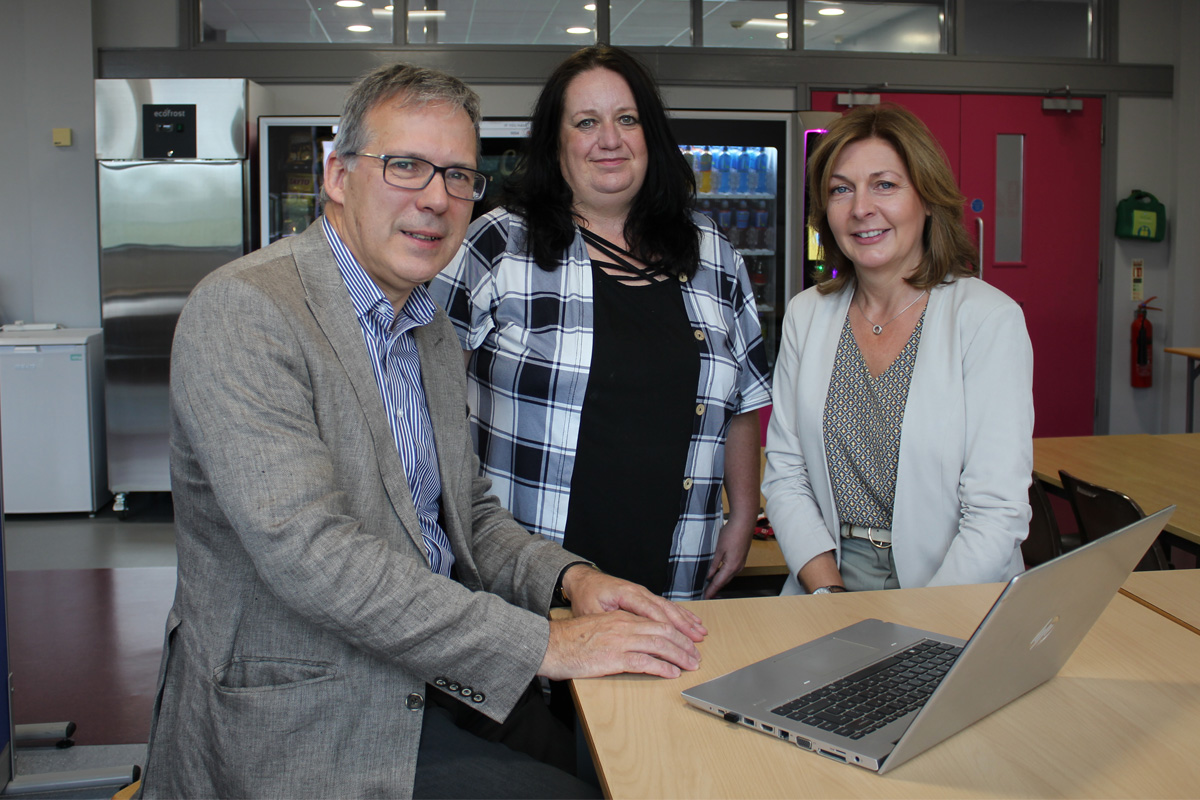 A man and two women in classroom setting at a desk with a laptop