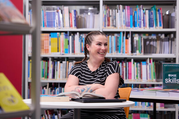 Woman sits at desk with arms folded and smiling in front of book shelf