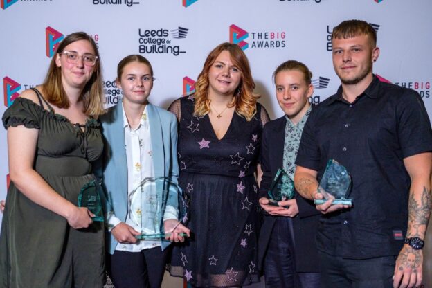 A group of male and female Leeds College of Building students pose in front of college banners with their glass trophies.