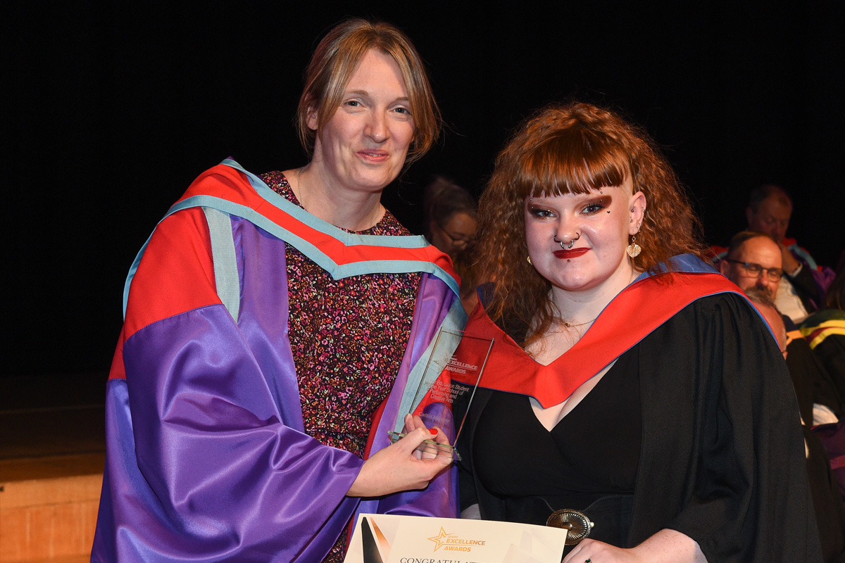 Two people in academic gowns, one presenting new graduate with award