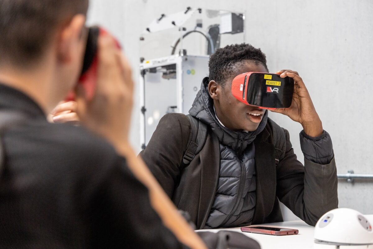 A student sits at a desk in a technology classroom wearing VR goggles.