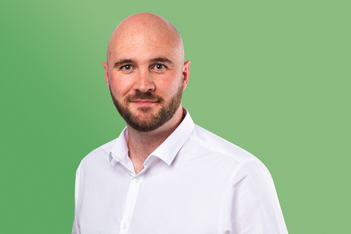 Man with brown beard and white shirt faces the camera smiling