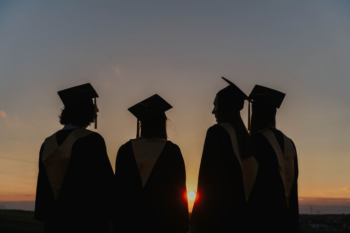 Four Graduates in their gowns and hats with a sunsetting behind them, pexels stock