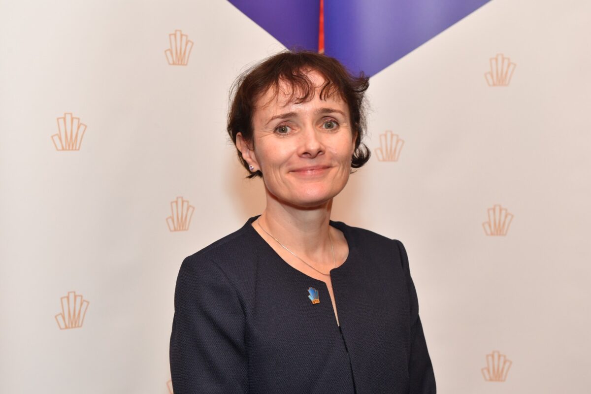 A woman dressed in a blue suit poses in front of a background decorated with the UTC 'intelligent hand' logo.