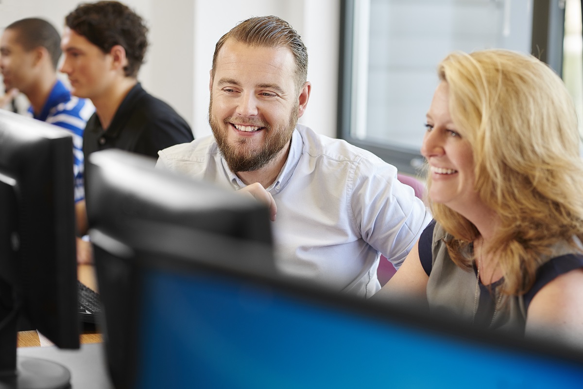 A woman sitting at a computer smiling while a man sits next to her, also smiling