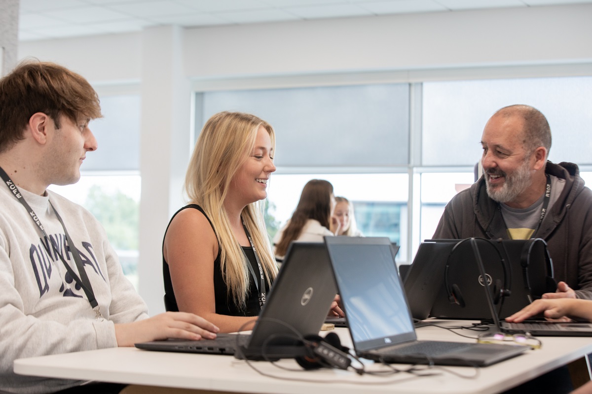 Three people of different ages smiling with laptops