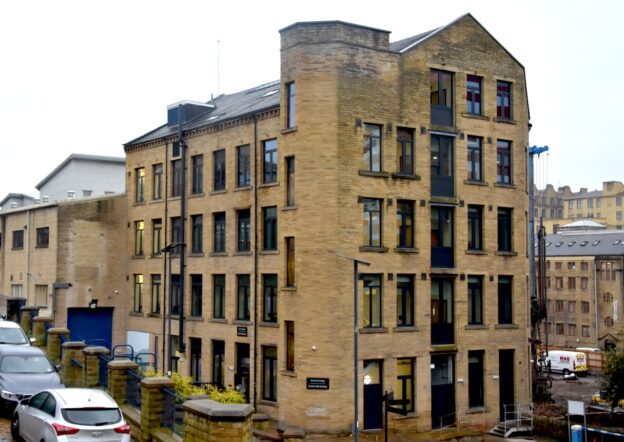 An external shot of the refurbished Garden Mills building. The brown stone mill building has modern black windows and doors.