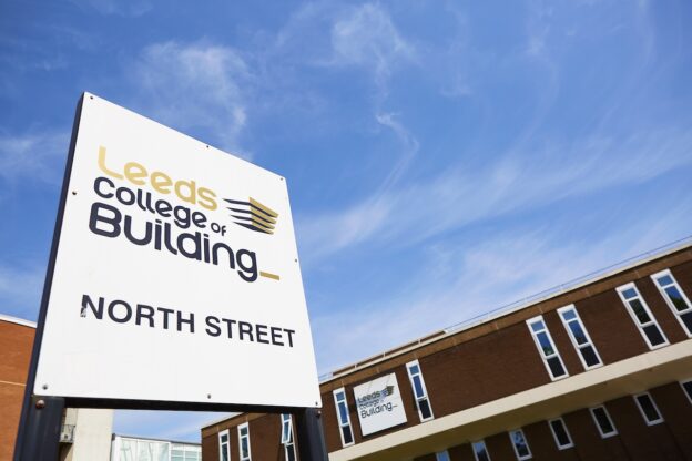 A Leeds College of Building North Street Campus branded sign stands in front of the campus building beneath a blue sky.