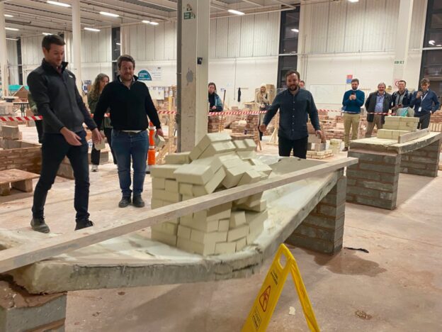 Three male engineers watch as large concrete slabs collapse in a demonstration held at the Leeds College of Building workshop.