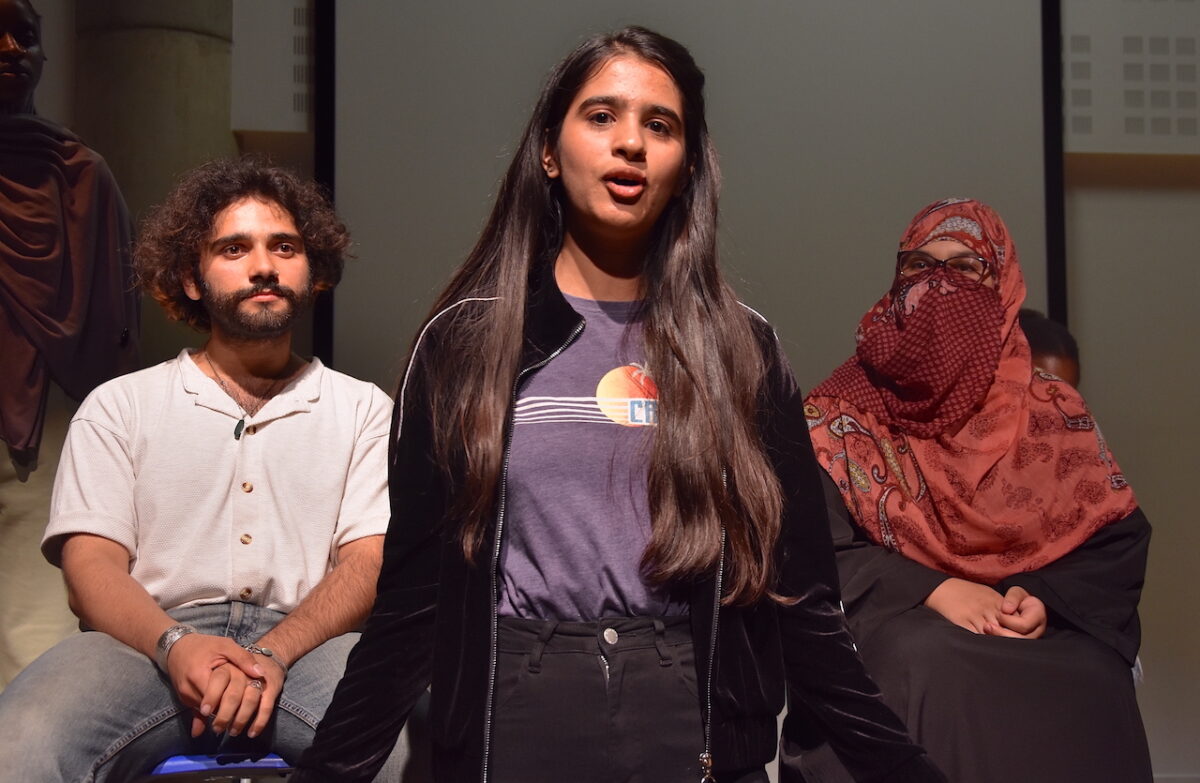 Three ESOL students perform on a stage for Refugee Week.