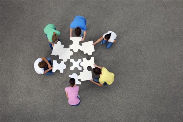 6 people in different coloured shirts putting together large jigsaw puzzle pieces