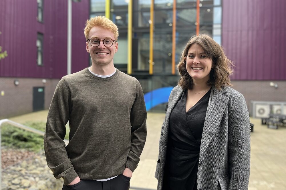 Two people standing and smilling outside a college building