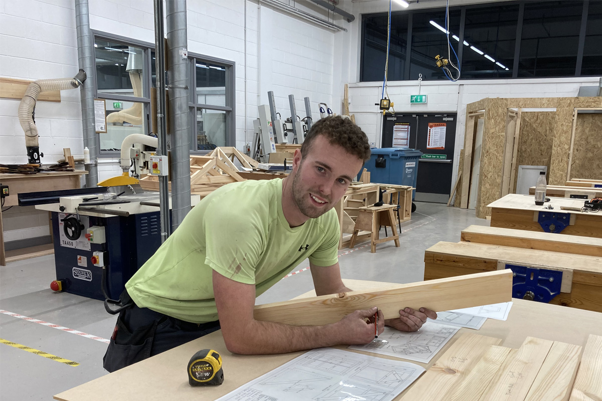 Male student leaning over plans in joinery workshop.