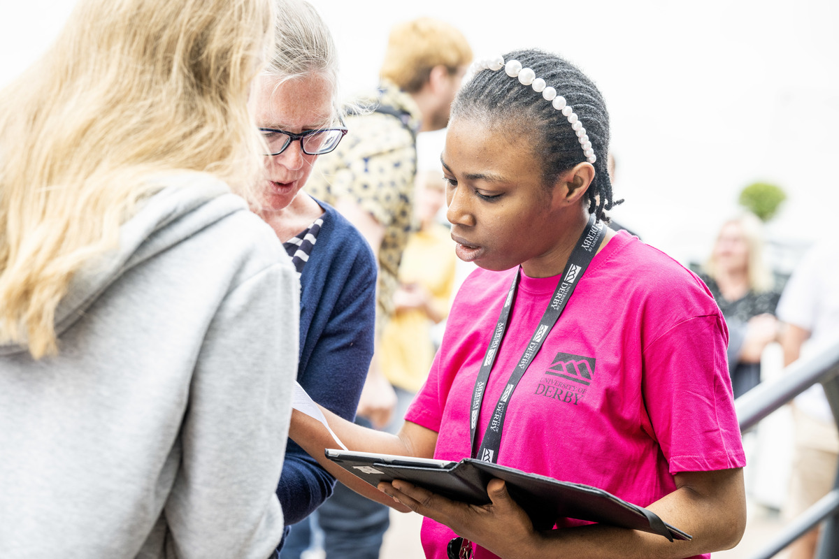 A woman wearing a University of Derby t-shirt is helping a prospective student