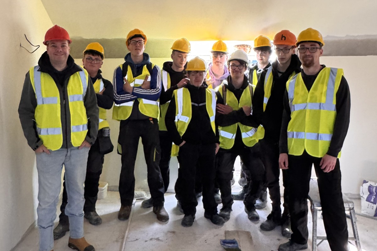 Group of students in high viz jackets and hard hats on building site.