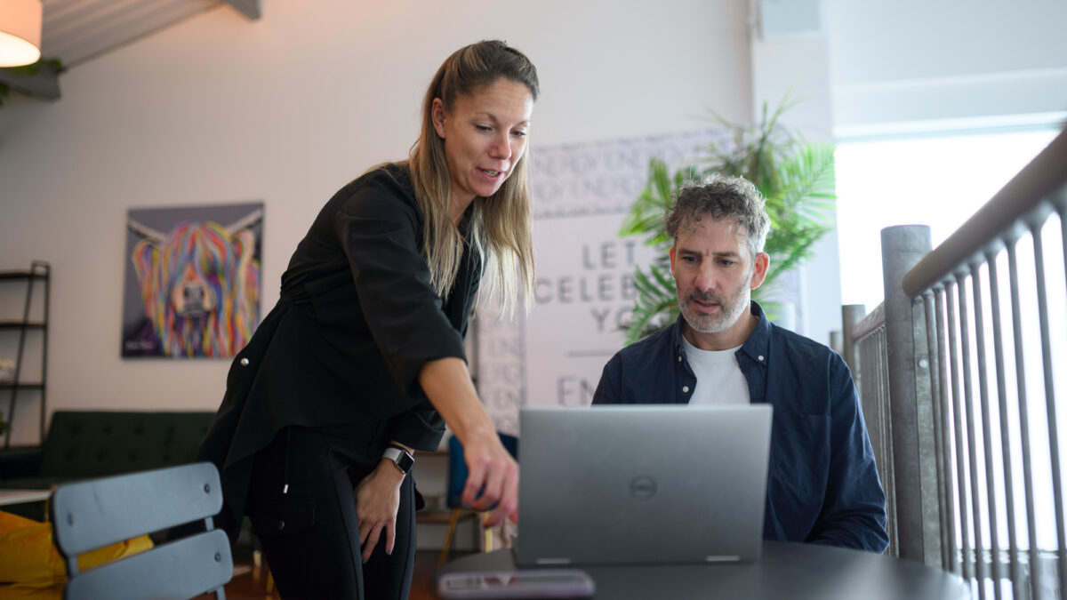 Two people working together on one laptop.