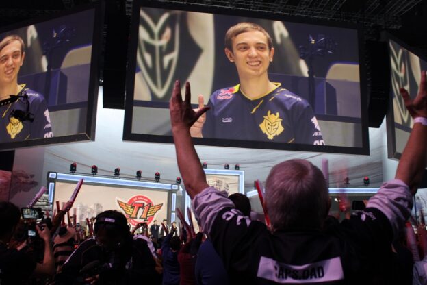 Esports championship with fan cheering, arms raised in the foreground and an esports player smiling on a big screen