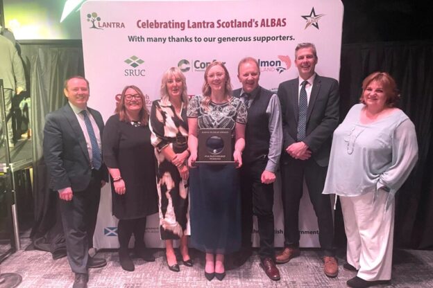 A group of seven people posing at the Lantra Scotland ALBAS awards event. They are standing in front of a backdrop featuring the Lantra logo and the words 'Celebrating Lantra Scotland’s ALBAS' along with sponsor logos.