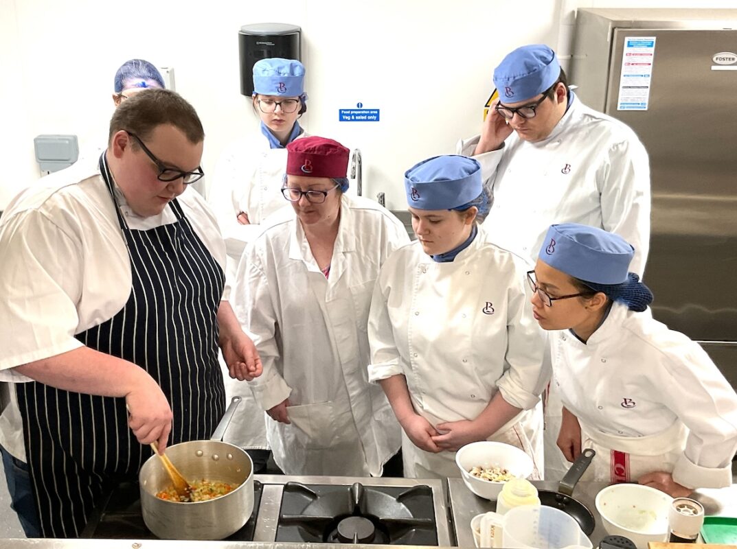 Group of students watching a cooking demonstration in a kitchen setting