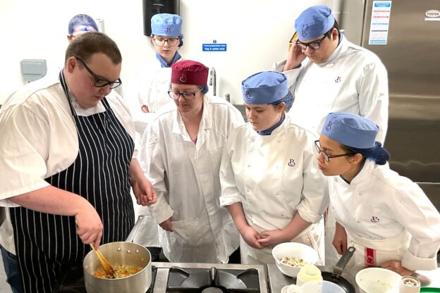 Group of students watching a cooking demonstration in a kitchen setting