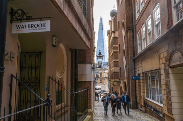 Image of a narrow street in central London. You can see the Shard through the gap at the end of the street. A hanging sign on a building on the left hand side reads "Walbrook Institute London"